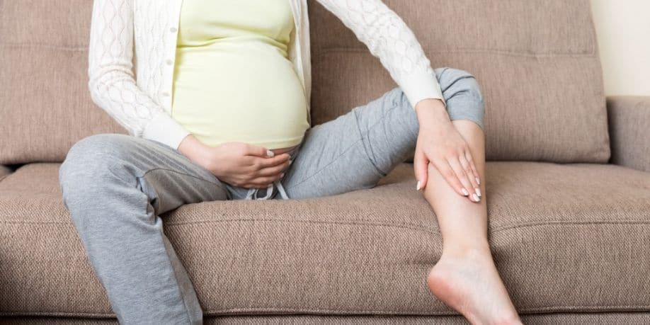 Manos masajeando el pie hinchado mientras está sentada en el sofá