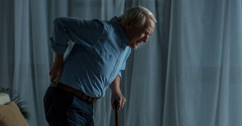 Hombre mayor que sufre de osteoporosis se apoya en un bastón