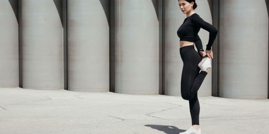 Mujer joven deportista calentando las piernas en la calle