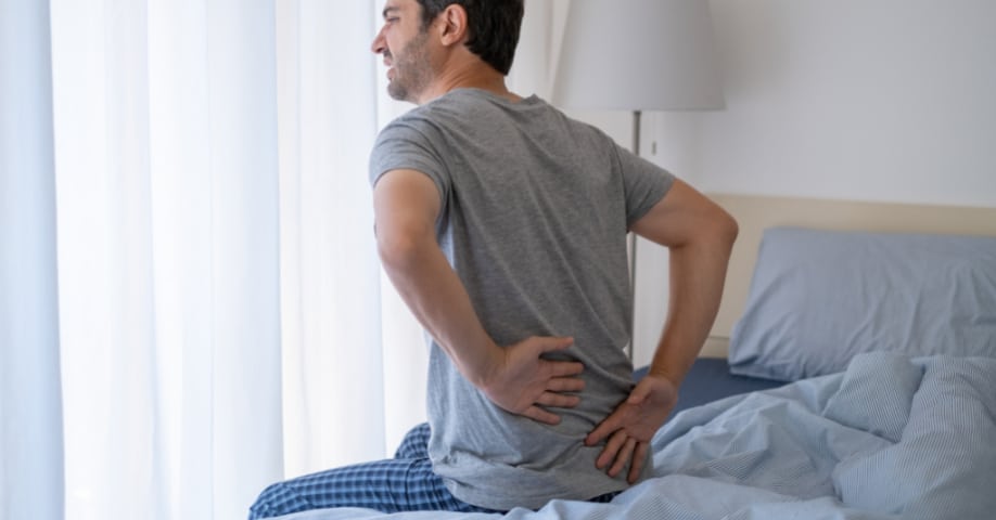 Hombre levantándose de la cama con dolor de espalda