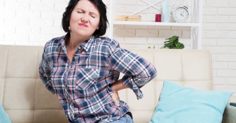 Mujer de mediana edad con dolor de espalda se sienta en el sofá